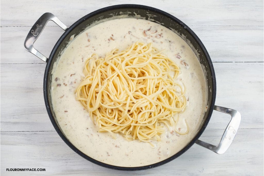 Adding pasta to Alfredo sauce in a skillet