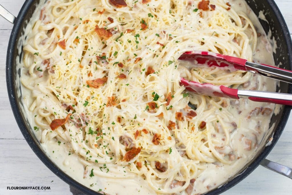 Homemade Smoked Gouda Alfredo Sauce mixed with cooked pasta, garnished with bacon and parsley in a large skillet before serving