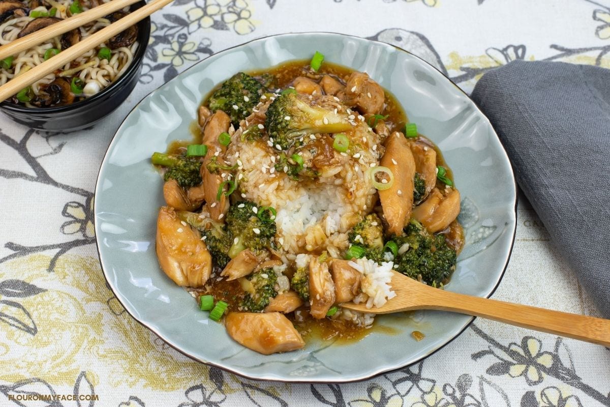 chicken and broccoli served over a mound of white rice with a bamboo forkful of the chicken