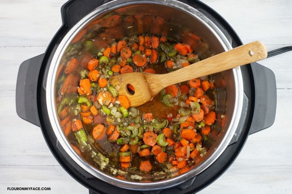 sautéed vegetables, herbs and spices covered with cooking win inside the pressure cooker pot.
