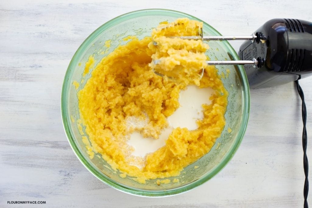 Adding cream to mashed rutabaga before beating in a large bowl.