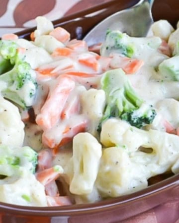 Mixed cauliflower, broccoli and carrots with a cream sauce served in a brown serving bowl.