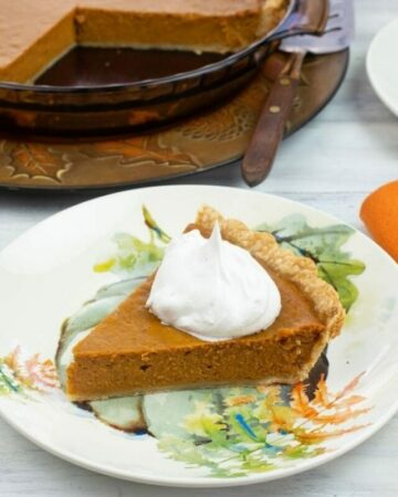 Sliced pumpkin pie topped with whipped cream on a plate.