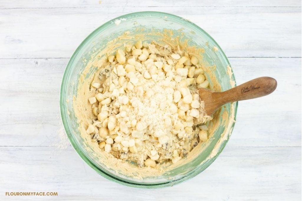 Adding chopped macadamia nuts to a bowl of cookie dough.