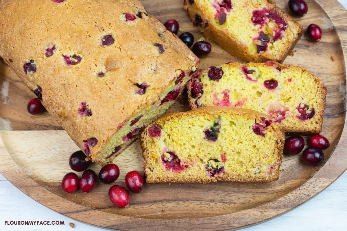 A loaf of cranberry breaded sliced on a wooden cutting board.