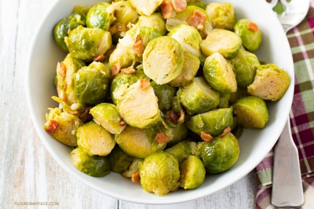 a white serving bowl filled with steamed Brussels Sprouts and bacon bits.