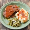 Sliced meatloaf, mashed potatoes, and green beans on a green dinner plate.