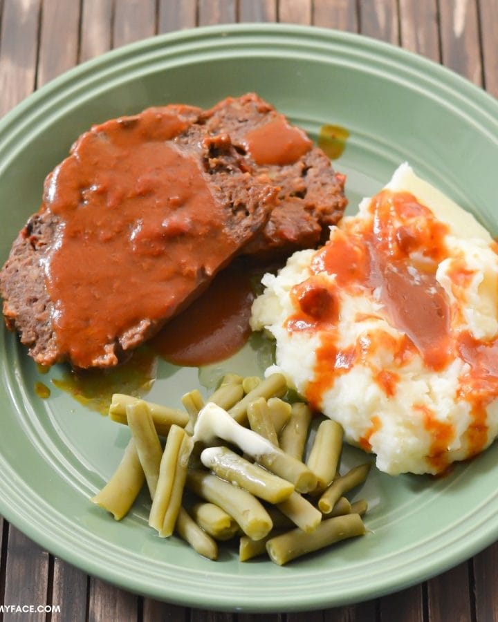 Sliced meatloaf, mashed potatoes, and green beans on a green dinner plate.