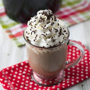 A mug of crock pot hot cocoa topped with whipped cream and sprinkles.