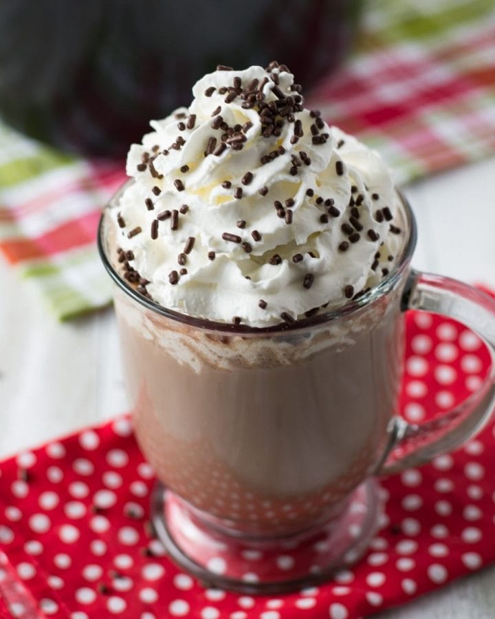 A mug of crock pot hot cocoa topped with whipped cream and sprinkles.