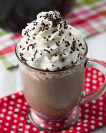 A mug of crock pot hot cocoa topped with whipped cream and sprinkles.