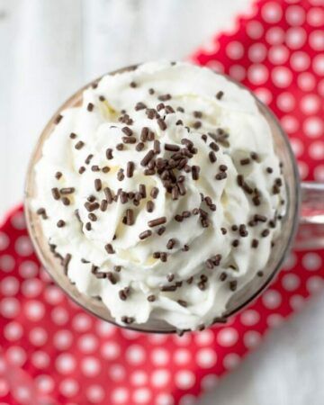 Overhead image of a mug of hot cocoa topped with w swirl of whipped cream and sprinkles.