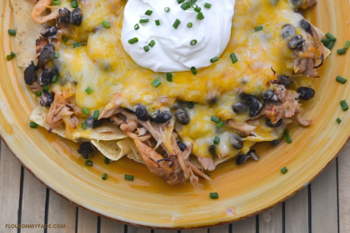 a plate of pulled pork nachos topped with melted cheese and a dollop of sour cream.