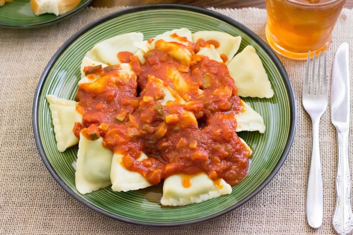 A dinner plate serving of ravioli with garden vegetable sauce.