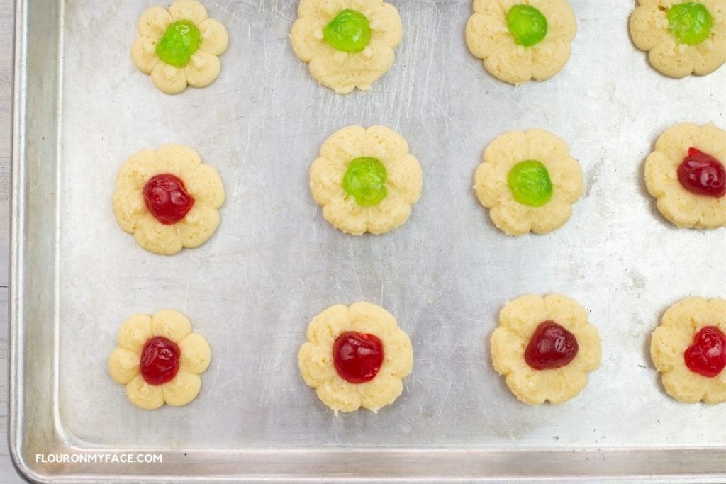Spritz cookies topped with candied cherries on a baking sheet.