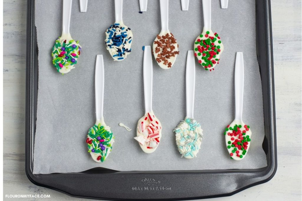 White chocolate dipped spoons decorated with sprinkles on a cookie sheet.