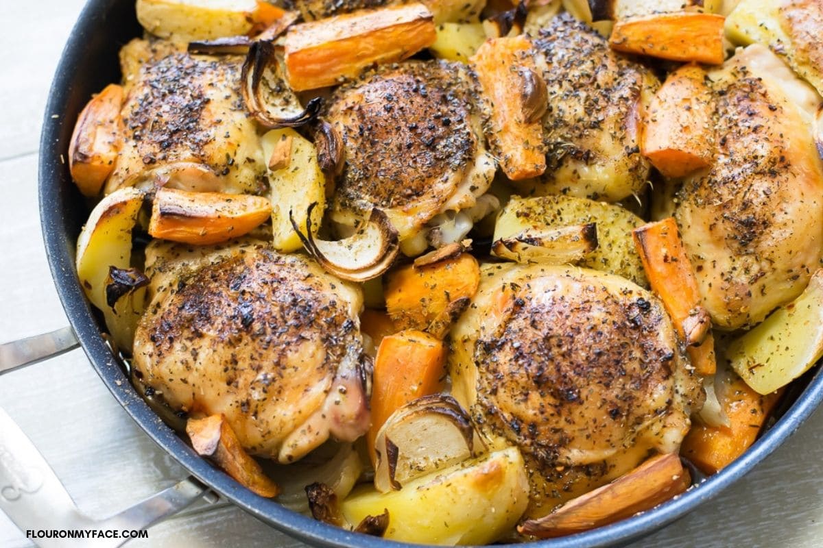 Greek chicken with potatoes and carrots in a skillet.