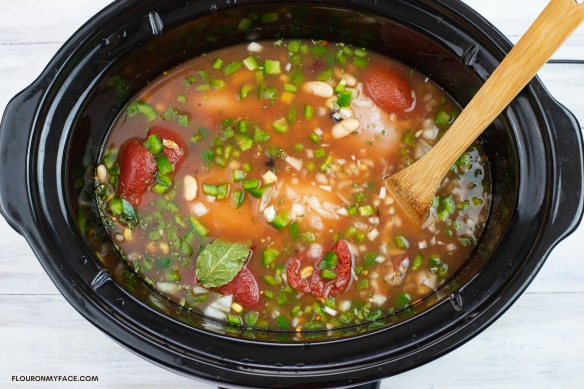 Chili ingredients floating in chicken broth in a crock pot.