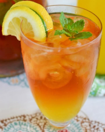 A tall glass filled with Mango Iced Tea with lemon slices and mint leaves garnish.