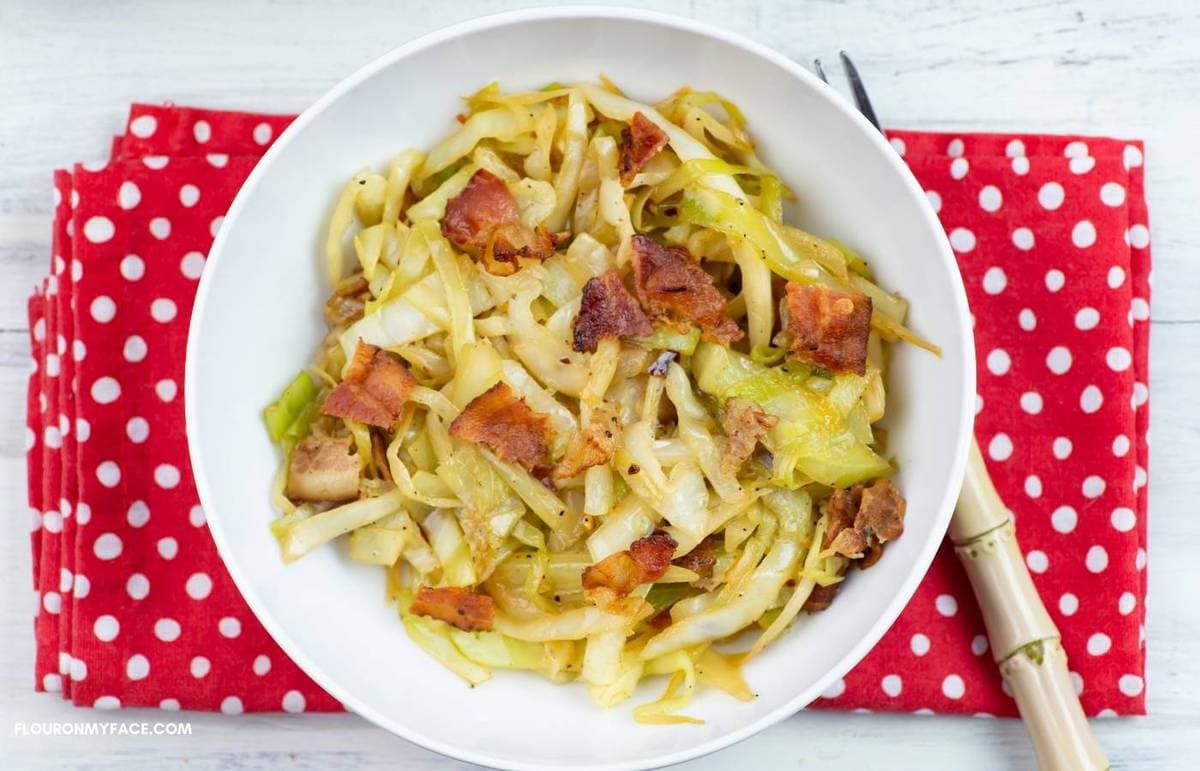 A bowl filled with fried cabbage and bacon on a red napkin.