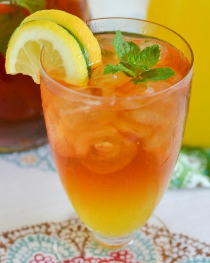 A tall glass filled with Mango Iced Tea with lemon slices and mint leaves garnish.