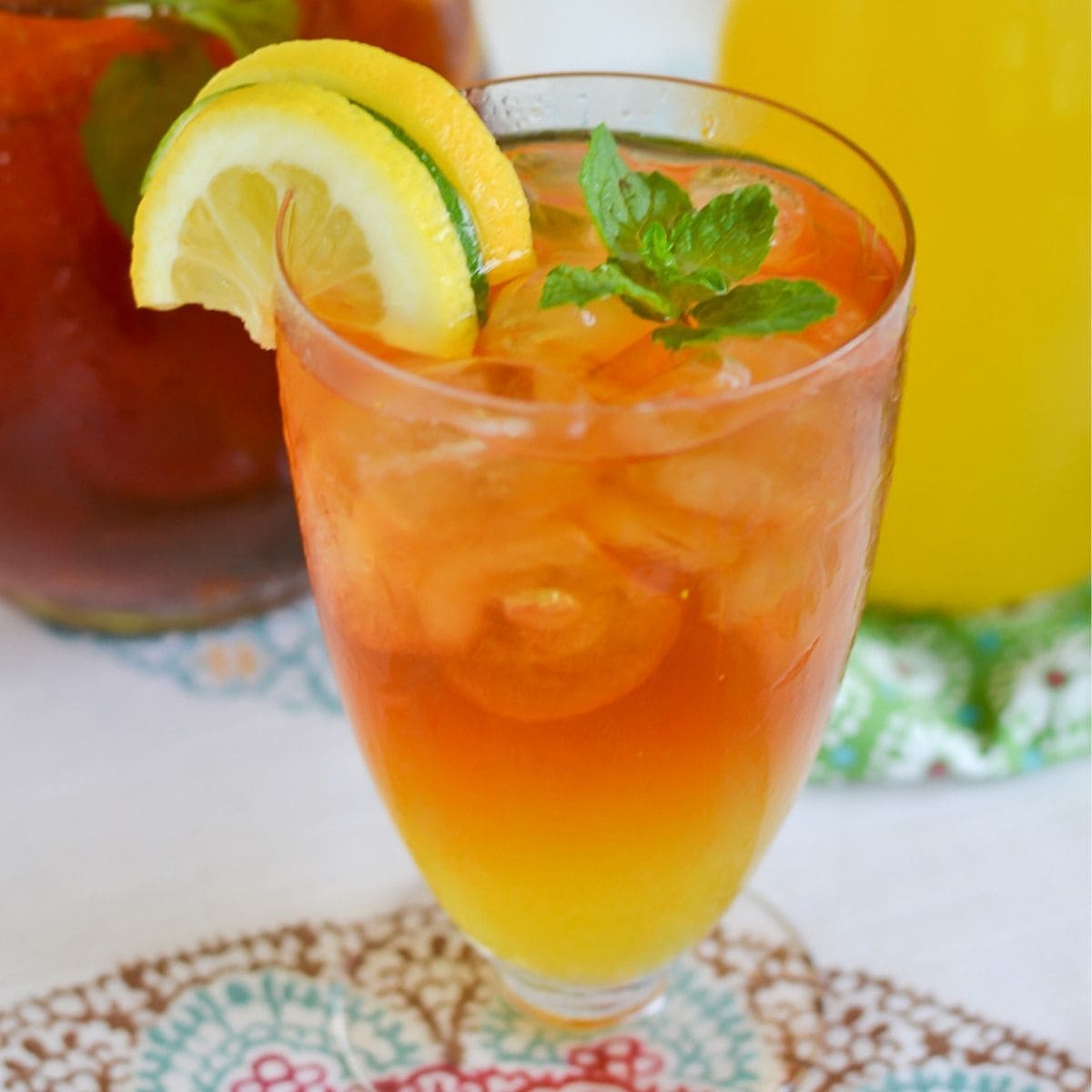 A tall glass filled with Mango Iced Tea with lemon slices and mint leaves garnish.
