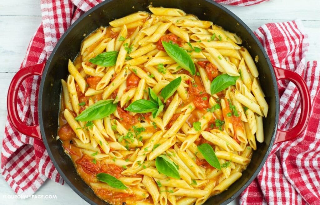 Pasta dotted with fresh basil in a skillet.