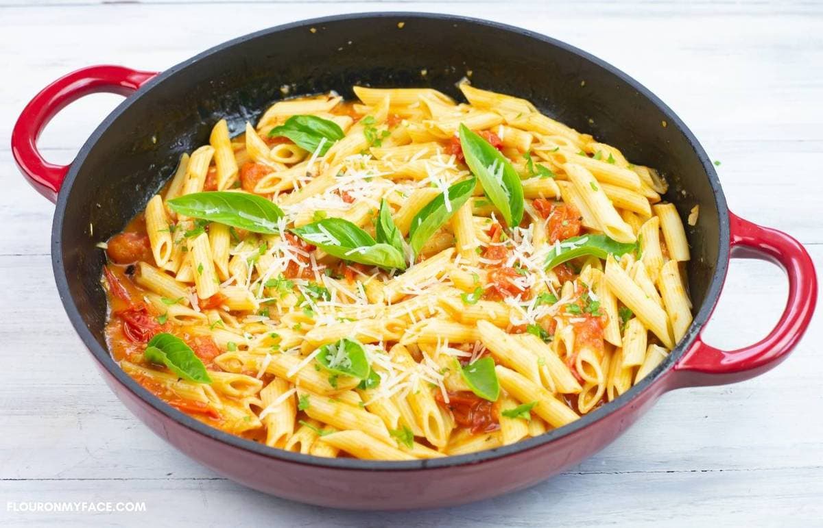 Pasta, sauce, basil leaves and Parmesan cheese in a red skillet.