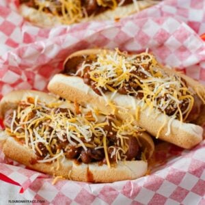 2 Chili Cheese Dogs on buns in a red plastic basket.