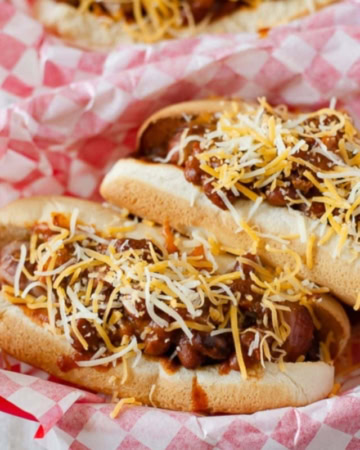 2 Chili Cheese Dogs on buns in a red plastic basket.