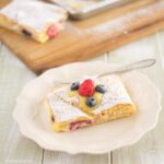 A lemon curd filled crescent bar topped with berries on a plate.