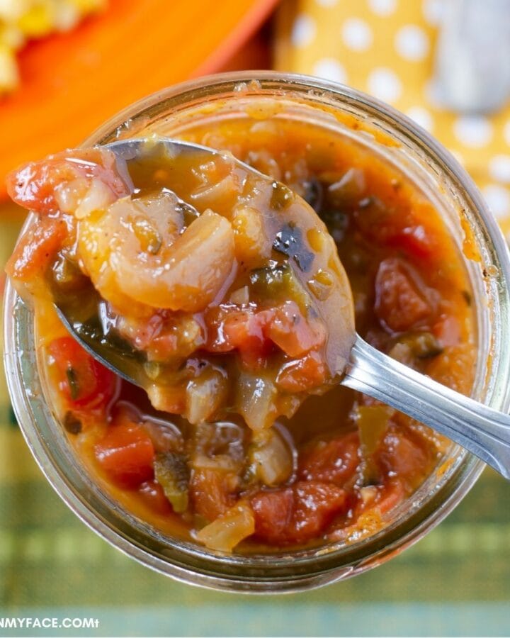Overhead image looking down into an open jar of roasted pepper peach salsa with a spoon rest ontop.