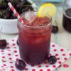 Sweet cherry iced tea served in a mason jar with a lemon wedge garnish.