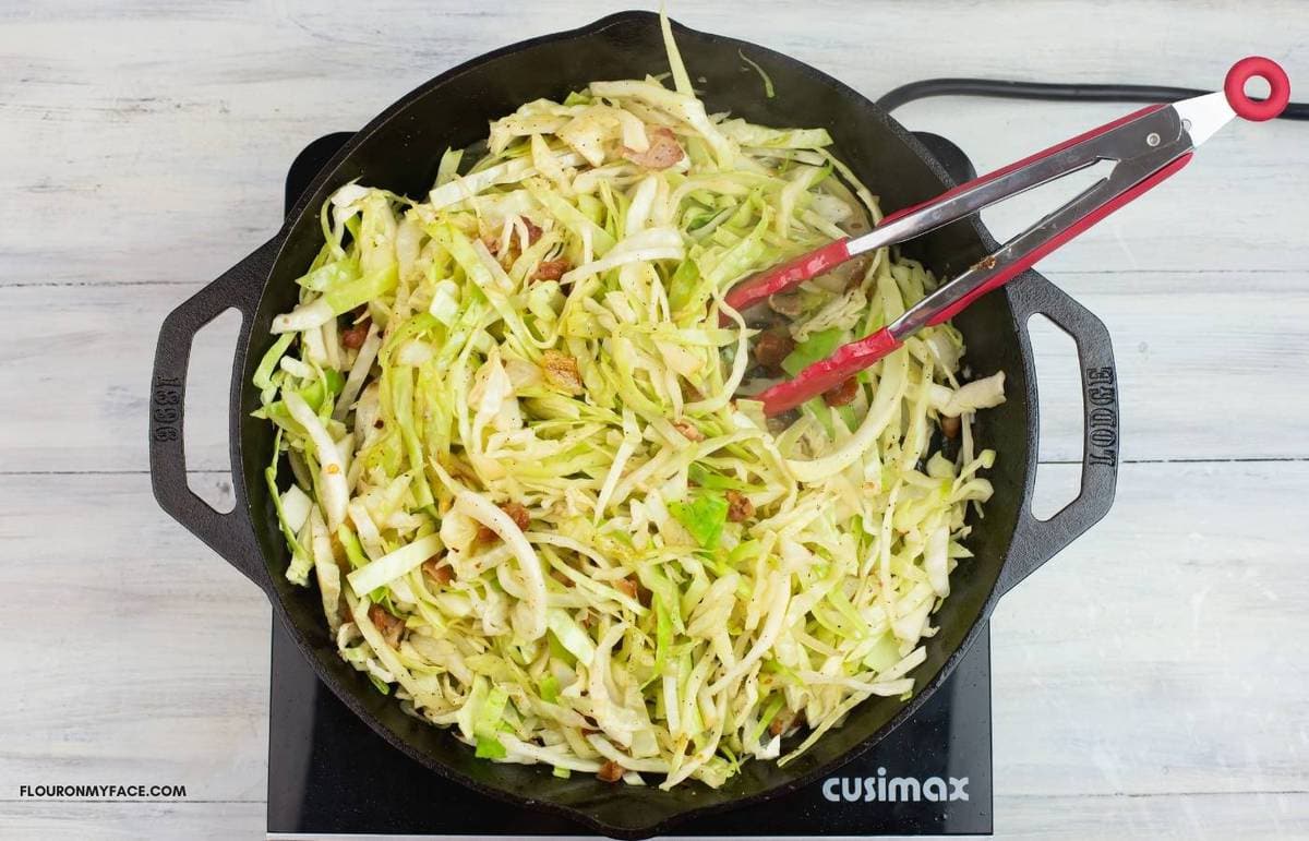 Tossing the cabbage with the seasonings in a skillet.