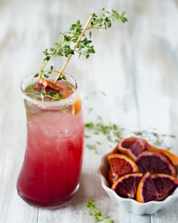 Blood Orange Thyme Paloma served in a tall glass with a sprig of thyme garnish.