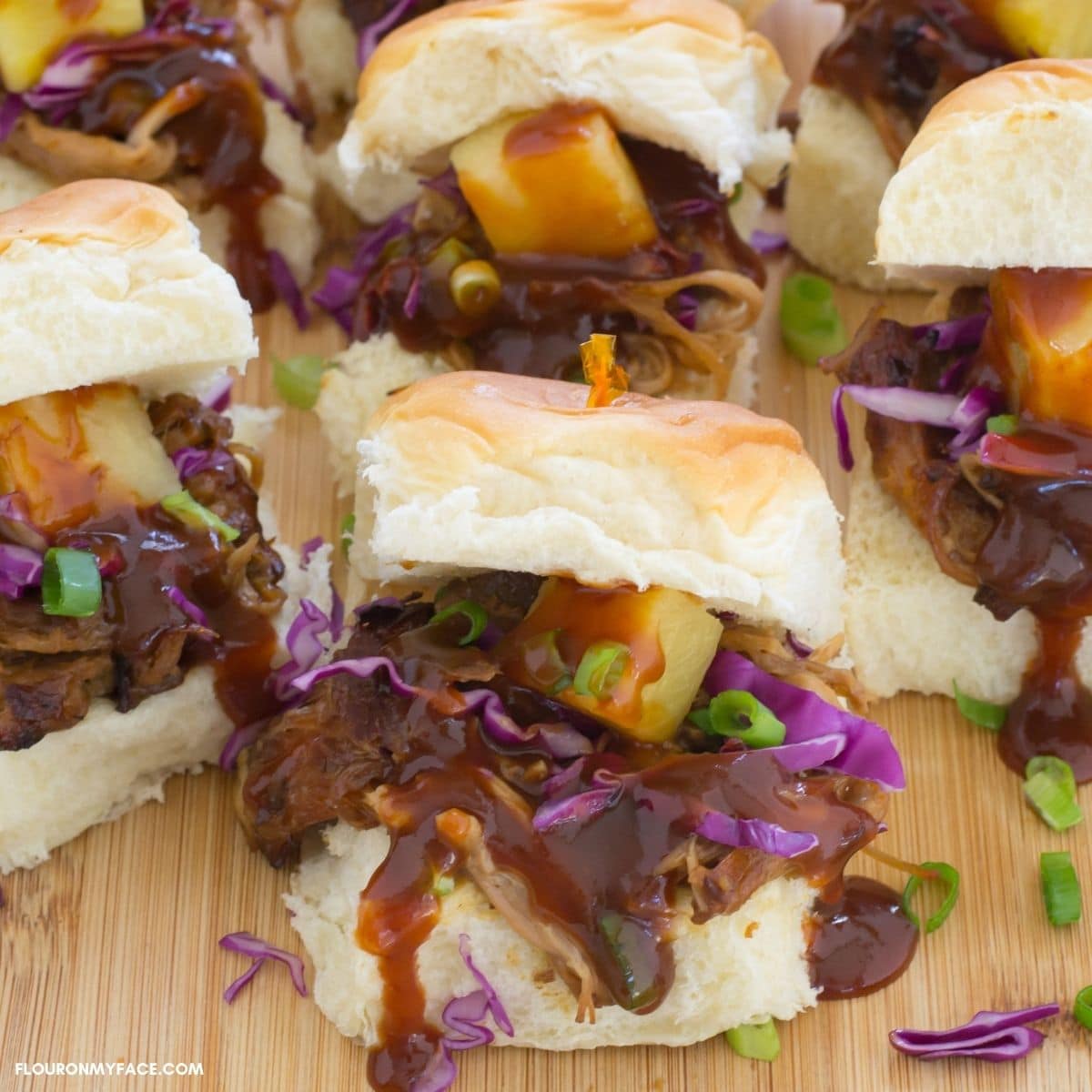 Pulled pork sliders topped with slaw on a cutting board.