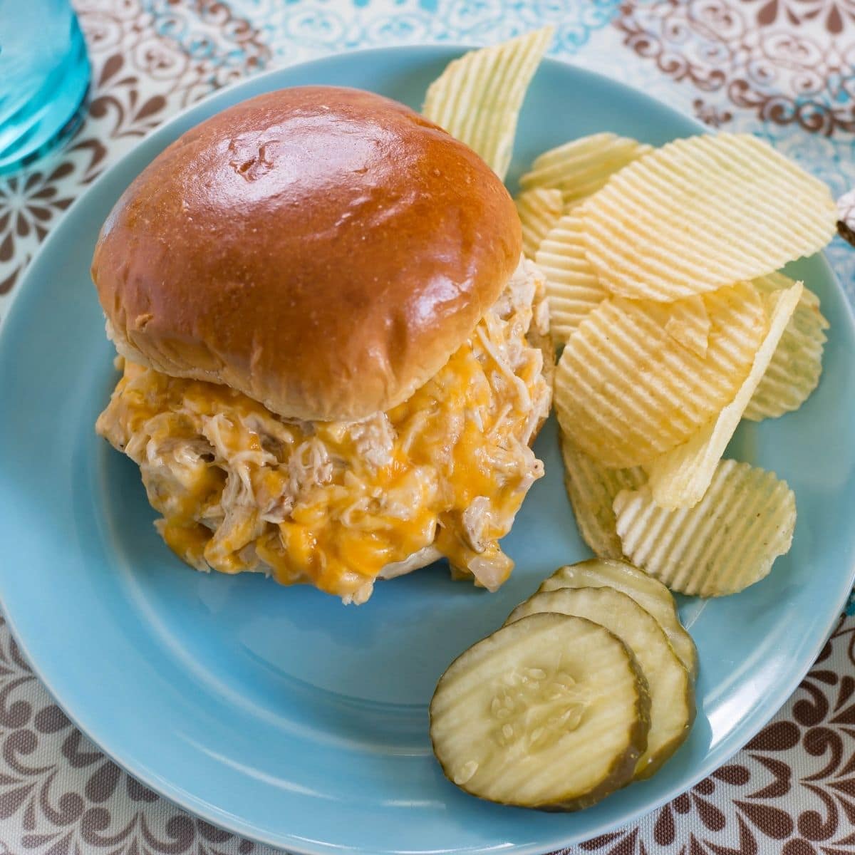 Cheesy chicken sandwich with chips and pickles on a plate.