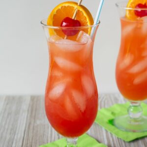 Classic Hurricane Cocktail served with ornage slice and cherry garnish in a hurricane glass.