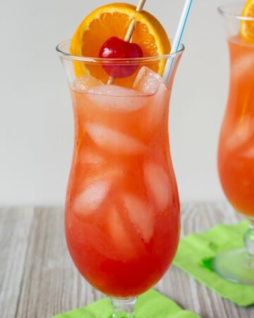 Classic Hurricane Cocktail served with ornage slice and cherry garnish in a hurricane glass.