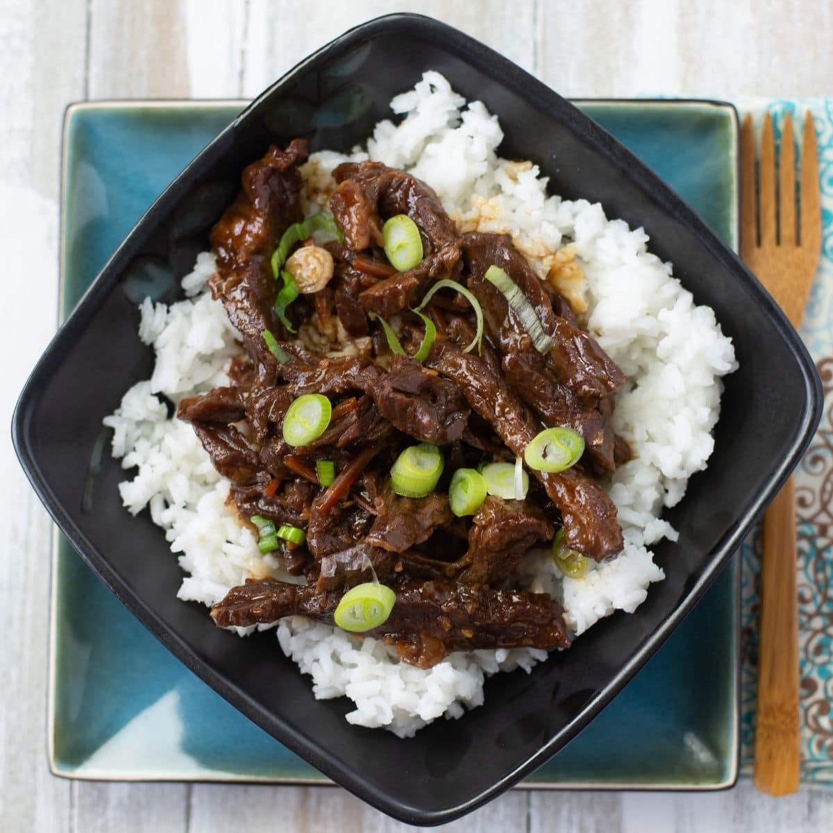 A square bowl with white rice and Mongolian Beef.