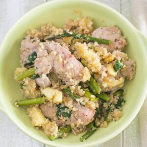A bowl filled with a serving of pork loin with spinach and asparagus over quinoa.