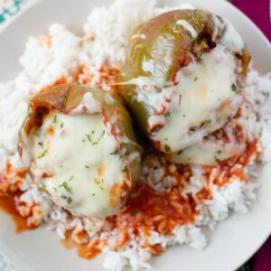 Two stuffed bell peppers on plate on a bed of cooked white rice.