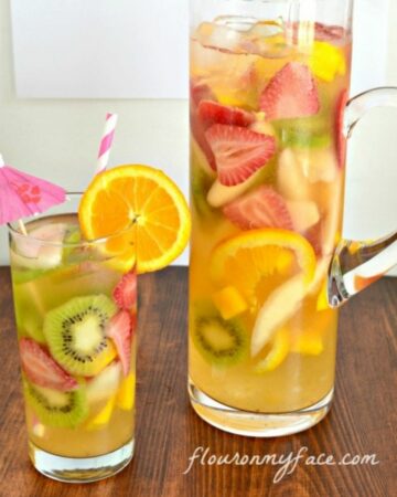 A glass and tall pitcher filled with White Moscato Sangria.