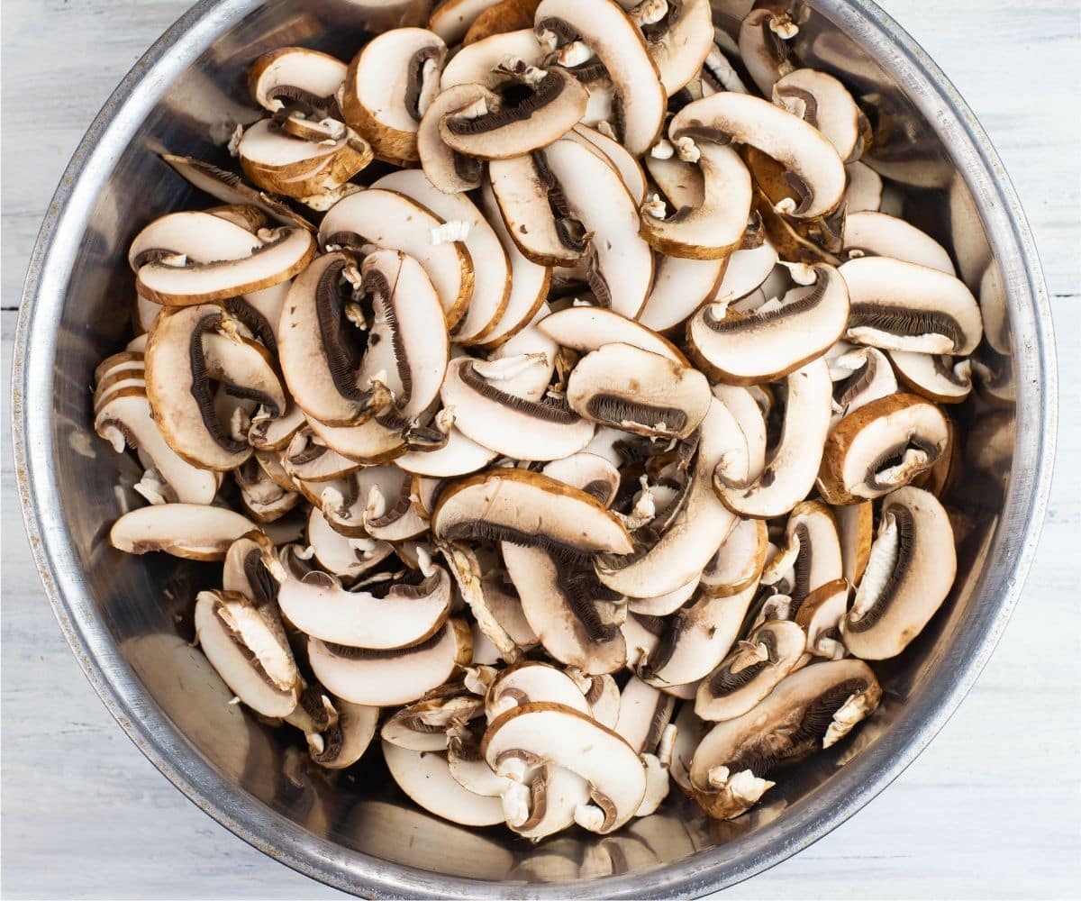 sliced baby bella mushrooms in a metal bowl.