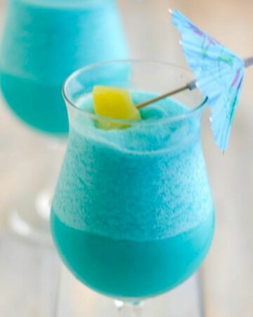 Blue Hawaiian Cocktail in a hurricane glass garnished with pineapple and umbrella.