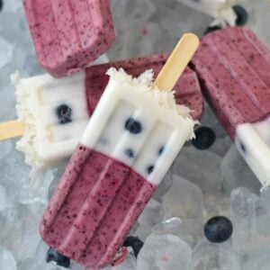 Layered blueberry coconut ice pops on a bed of ice cubes.
