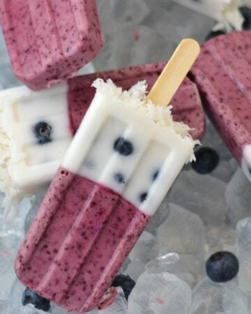 Layered blueberry coconut ice pops on a bed of ice cubes.