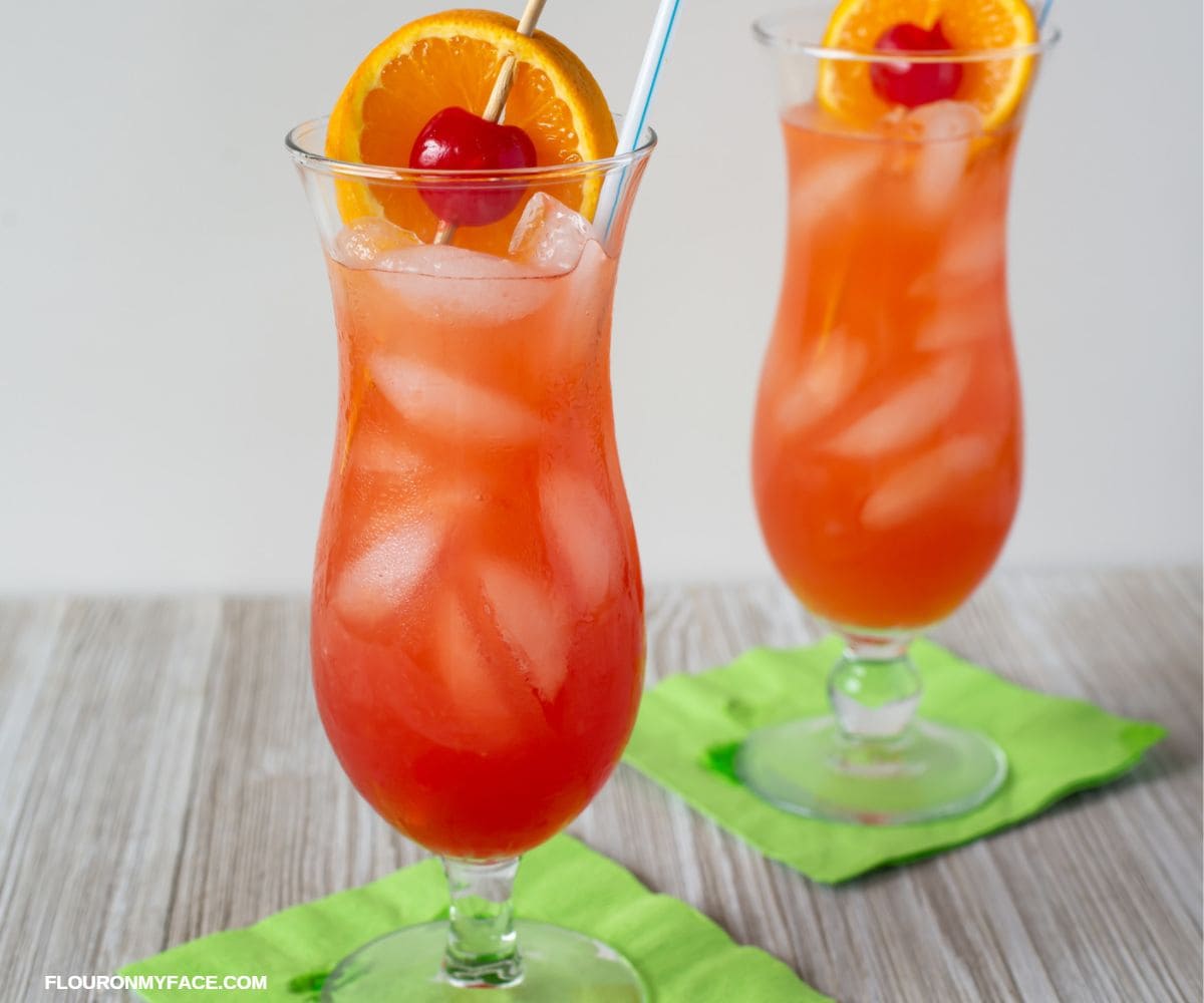 Two hurricane glasses filled with the classic hurricane cocktail, garnished with a cherry and slice of orange.