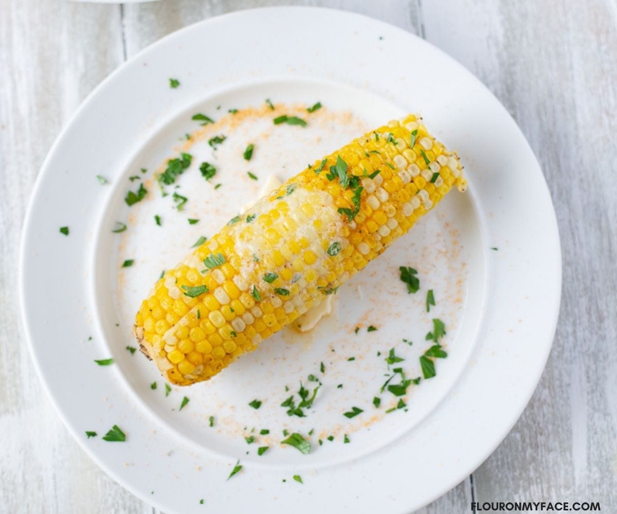 An ear of corn with melted butter on a white plate.