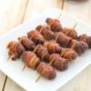 A white serving dish with bacon wrapped cocktail weenies.